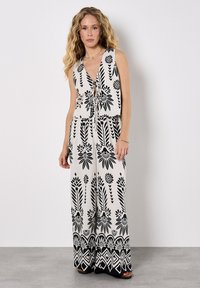 Combinaison sans manches en crème avec des motifs floraux et géométriques noirs ; présente un décolleté en V et une fermeture par nœud à la taille.