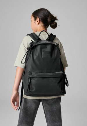 Černý nylonový batoh s zaobleným designem, přední kapsou na zip, nastavitelnými popruhy a texturovaným logem na přední straně.