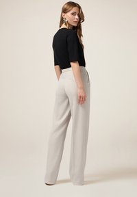 Zwarte, korte mouw top gecombineerd met lichtgrijze, hoge taillebroeken. De broeken hebben een gladde textuur en een elastische taille. Opvallende oorbellen.