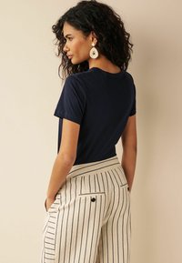 Marineblauwe T-shirt met korte mouwen gecombineerd met crèmekleurige en marineblauwe gestreepte highwaisted broek met achterzakken en knoopdetails.