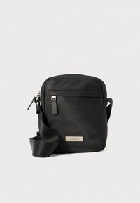 Sort nylon crossbody taske med rektangulær form, justerbar rem, forreste lynlåsrum og sølvlogo-plade på siden.