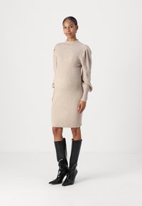 Strikket beige kjole med ribbet tekstur, lange puffarmer og høy hals. Kombinert med svarte knelang støvler med spiss tå.