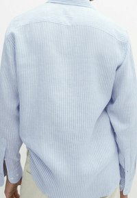Camicia azzurra a maniche lunghe con righe verticali bianche, colletto button-down e orlo curvato. Il tessuto sembra morbido e testurizzato.