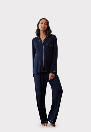 Marineblauwe pyjama set met een knoopsluiting bovenstuk met een zak en witte bies, gecombineerd met losse, bijpassende broek. Zacht materiaal, comfortabele pasvorm.