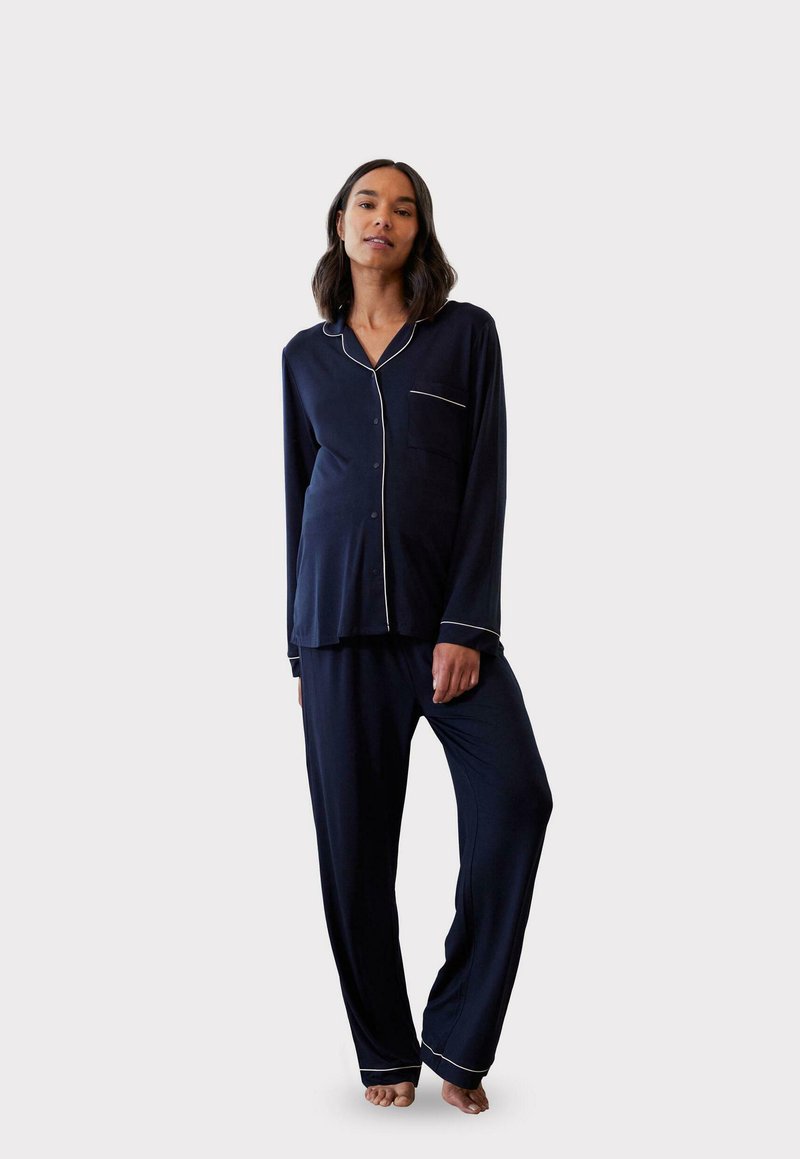 Granatowy zestaw piżamowy składający się z koszuli zapinanej na guziki z kieszonką i białymi lamówkami, w komplecie z luźnymi spodniami w tym samym kolorze. Miękka tkanina, swobodny krój.