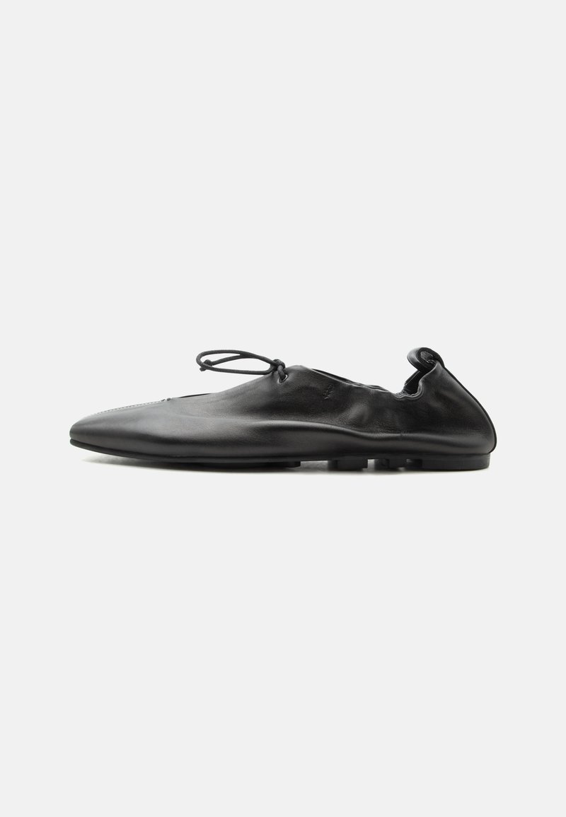 Chaussure plate en cuir noir avec bout arrondi, dos élastique et fine lacet noué au-dessus du cou-de-pied, vue de profil sur fond blanc.