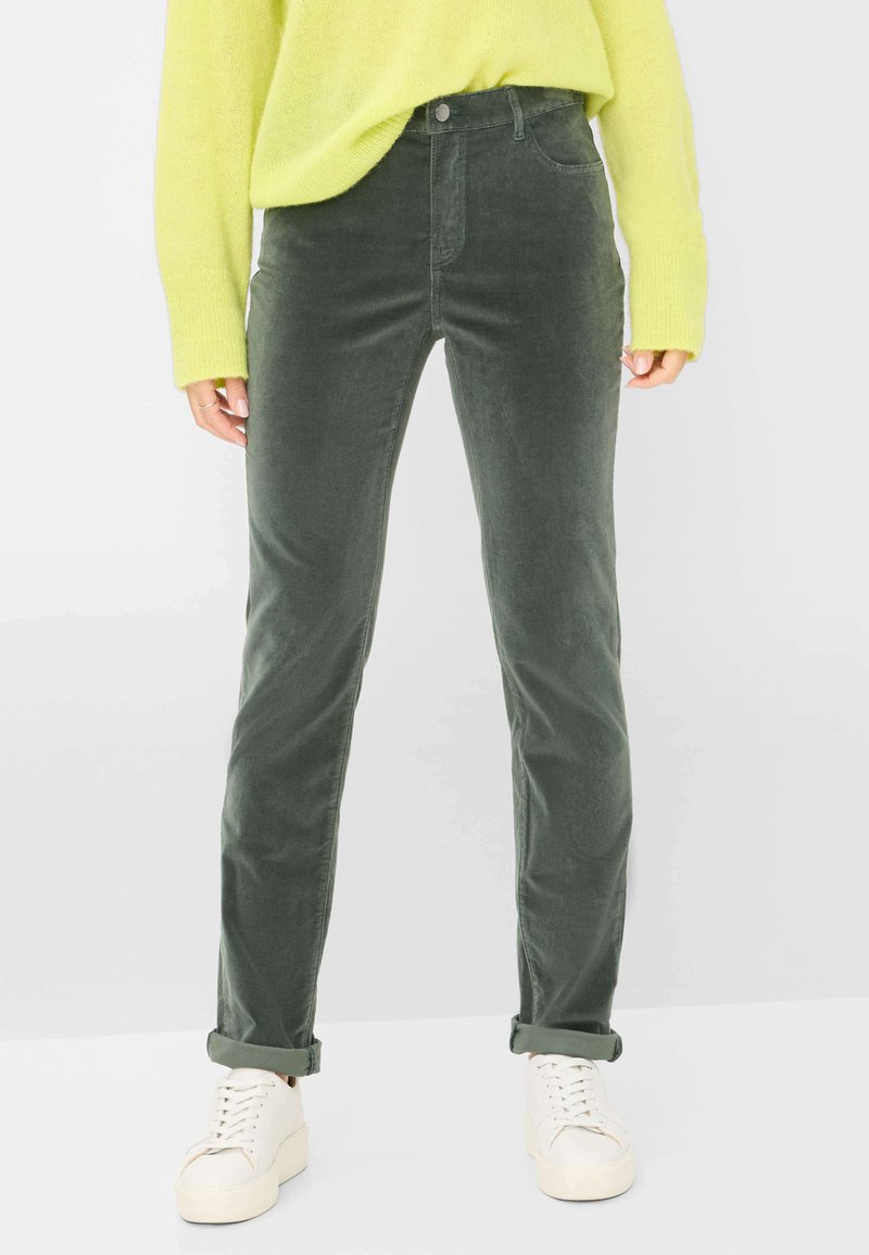 Olivenfarvede fløjl bukser med lige pasform, der har forlommer, opsmøgede ærmer og er parret med hvide lavtop sneakers.