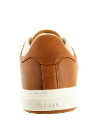 Adidași din piele maro cu talpă din cauciuc albă, având o textură netedă, un design rotunjit și un branding subtil pe călcâi.