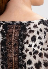 Průhledná blůza s černými krajkovými detaily a leopardím potiskem. Měkká tkanina s mírně průsvitnou texturou na zadní straně.