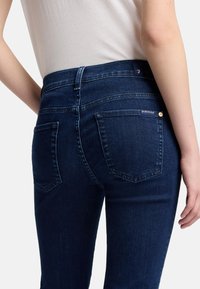 Donkerblauwe denim jeans hebben een slim fit ontwerp, een middelhoge tailleband en twee achterzakken met stikseldetails.