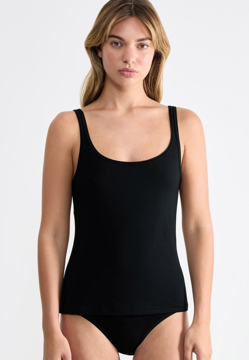 Black tank top with a scoop neckline, made of smooth fabric. Features thin straps and a fitted design, paired with black underwear.