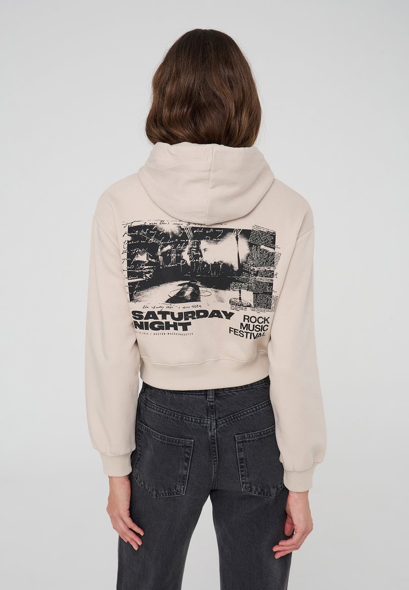 Przycięta beżowa bluza z kapturem z graficznym nadrukiem "FESTIWAL MUZYKI ROCKOWEJ W SOBOTNIA NOC", miękka w dotyku, z doszywanym kapturem.