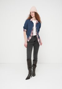 Μπλε πλεκτή ζακέτα πάνω από κόκκινο και λευκό καρό πουκάμισο, λευκό μπλουζάκι, γκρι τζιν και ψηλές μαύρες μπότες με τακούνι· ανοιχτό ροζ σκουφί.