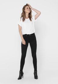 Sorte skinny jeans med paneldetaljer, sammen med en løs hvit t-skjorte. Outfitet inkluderer svarte hælankelstøvler.