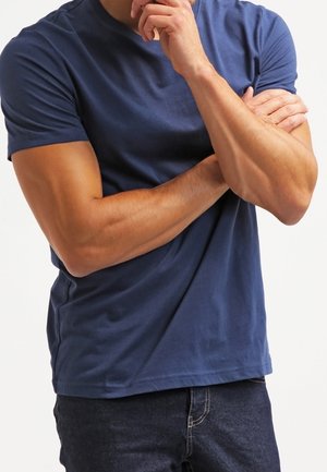 Marineblaue kurzärmlige T-Shirt aus weichem Stoff, mit klassischem Rundhalsausschnitt. Kombiniert mit dunklen Jeans.