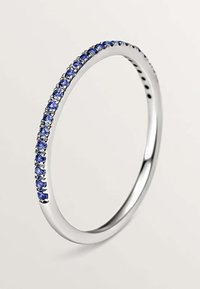 Anillo de plata con una banda redonda y lisa, que presenta una fila de piedras preciosas azules engastadas a lo largo de la superficie. Acabado pulido, diseño minimalista.