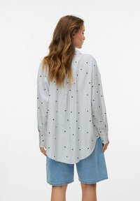 Wit gestreepte shirt met groene hartafdrukken, met knoopkraag, lange mouwen en een afgeronde zoom, gecombineerd met blauwe denimshorts.