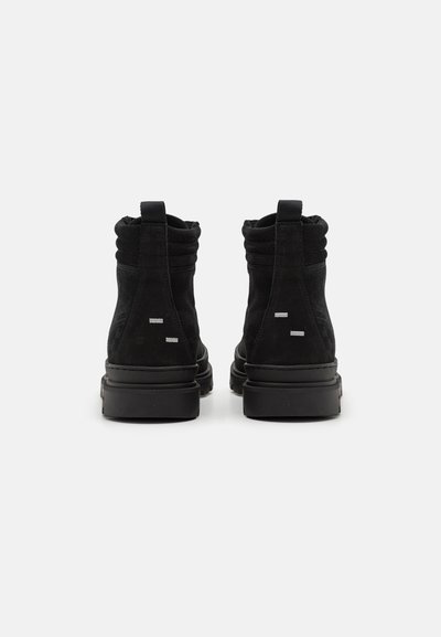 Bottes ankle en daim noires avec un bout arrondi, un col flexible et une semelle en caoutchouc. Détails de marque subtils en argent sur le talon et le côté.