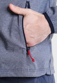 Gray zip-up jacket with a red drawstring detail, featuring a side pocket and textured fabric visible on the hand.