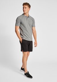 Polo shirt grigio a maniche corte abbinato a pantaloni shorts neri. Gli shorts presentano dettagli rossi e tasche, completati da scarpe sportive nere.