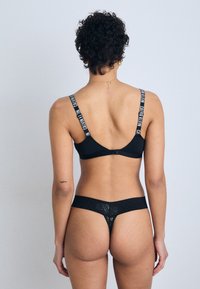 Black lingerie set featuring a bra with logo straps and a thong with a textured waistband, showcasing a simple, minimalistic design.