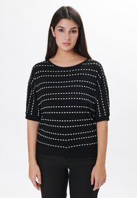 Pull en maille noir avec des rayures blanches en pointillés, encolure large et manches courtes. Texture douce et coupe décontractée. Assorti à un pantalon noir.