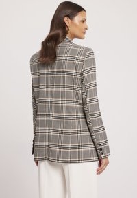 Marynarka w kratę w kolorze czarnym, beżowym i białym, z dopasowanym krojem, klapami w kształcie litery "notch" oraz zapięciem na guziki na mankietach. Gładka tekstura z wyraźną strukturą.