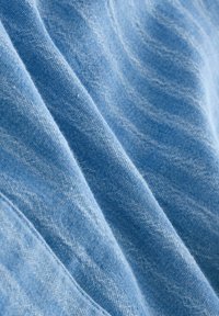 Textile bleu clair avec une texture tissée douce, affichant des variations subtiles de couleur et de motif. Les couches créent des plis et des drapés délicats.
