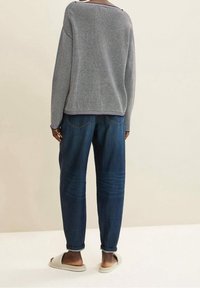 Grau gestrickter Pullover mit lockerer Passform, kombiniert mit dunkelblauen Jeans im lässigen Design. Hellgraue Slipper.