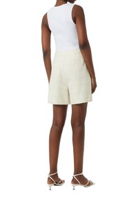 Weißes geripptes Tanktop kombiniert mit cremefarbenen, strukturierten Shorts mit Seitentaschen. Modell trägt weiße Sandalen mit Absatz und Riemchen.