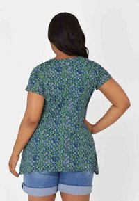 Blommig tunika i blått och grönt, med korta ärmar, rundad nederkant och en lös passform. Bärs tillsammans med uppvikta denimshorts.