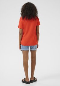 Oranžové tričko s krátkými rukávy, volný střih, doplněné o světle modré roztrhané džíny. Černé ploché sandály dotvářejí celý outfit.