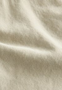 Jasno beżowy, textured materiał z delikatnym wzorem tkanym, pokazujący fale i miękkie fałdy. Odpowiedni do tapicerki lub odzieży.