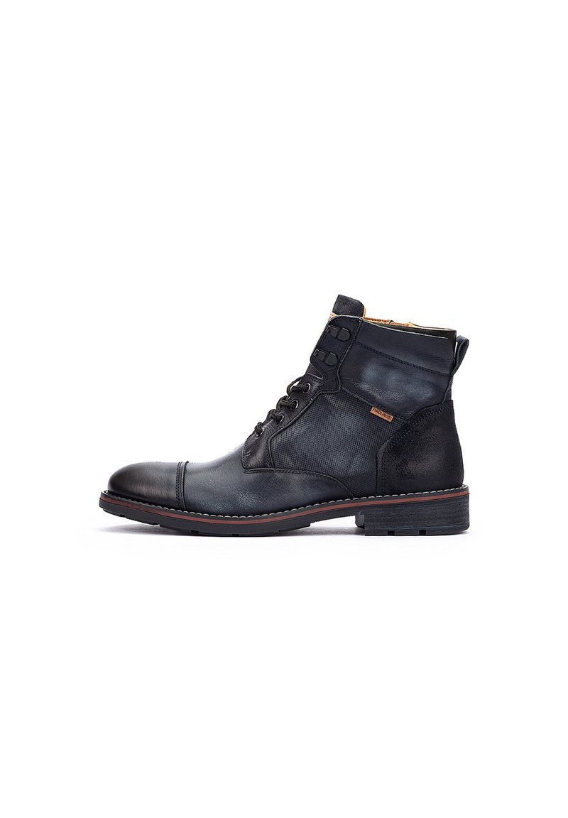 Botín de cuero negro hasta el tobillo con un acabado suave, puntera redonda, costuras en contraste y diseño de cordones. Cuenta con acentos de tela texturizada.