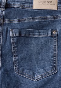 Jeans de mezclilla azul con un bolsillo trasero derecho que presenta costuras en contraste y una etiqueta de cuero que dice "STREET ONE" encima del bolsillo.