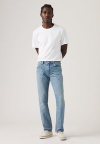 Λευκό βαμβακερό t-shirt, κλασική εφαρμογή, συνδυασμένο με ανοιχτόχρωμο μπλε τζιν παντελόνι. Η casual αθλητικά παπούτσια ολοκληρώνουν το σύνολο, με ουδέτερο φόντο.