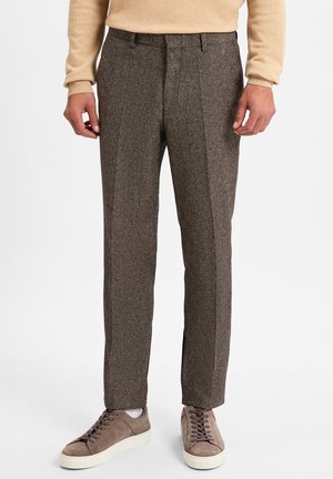 Braune Tweed-Hosen mit strukturierter Oberfläche, ausgestattet mit einem taillierten Schnitt und vertikalen Vorderfalten, kombiniert mit grauen Wildledersneakern.