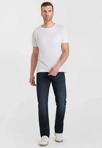 T-shirt blanc à manches courtes avec une poche, associé à un jean bleu foncé et des baskets blanches, présentant un design épuré et décontracté.