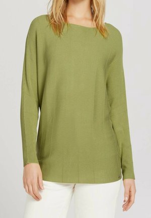 Maglietta verde a maniche lunghe con scollo a barca, tessuto texture, e una vestibilità ampia, abbinata a pantaloni chiari.