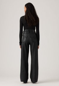 Zwarte, wijde denimbroek met hoge taille, subtiele achterzakken en een gladde textuur.
