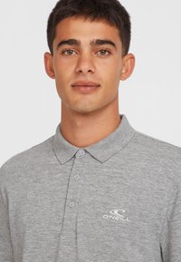 Polo gris avec un col, patte de boutonnage à trois boutons et logo O'Neill brodé en blanc sur la partie gauche de la poitrine.