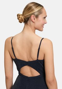 Abito blu navy con spalline sottili, tessuto testurizzato con una leggera scintilla e schiena aperta con dettaglio di chiusura a bottone.