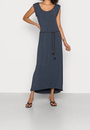 Woman wearing a sleeveless dark blue maxi dress with a braided belt and black strappy sandals, standing against a plain background.