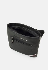 Borsa in pelle nera con superficie texturizzata, tasca frontale con zip e logo del marchio in rilievo. Presenta un accento a strisce in contrasto alla base.