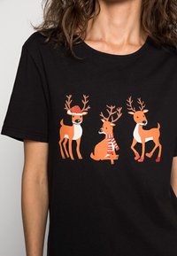 Svart T-shirt med tre tecknade renar: en med röd hatt, en i randig halsduk och en som står, alla i orange och vitt.