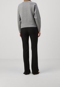 Felpa grigia con scollo rotondo a coste, abbinata a pantaloni neri svasati con una texture liscia e cuciture verticali.