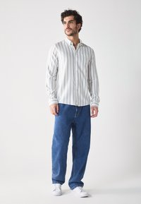 Gestreepte langwerpige shirt in grijs en wit met een knoopsluiting kraag, gecombineerd met losse blauwe denim jeans en witte sneakers.