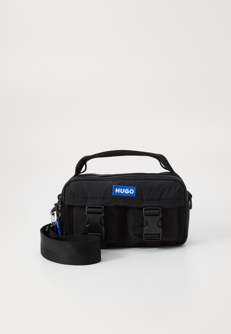 Black nylon bag with dual side buckles, a top handle, and an adjustable shoulder strap. Features a blue "HUGO" logo on the front.
