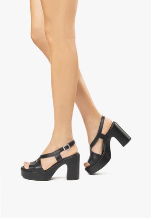 Sandali platform neri con design open-toe, cinturino alla caviglia regolabile con fibbia in argento e tacco spesso e alto. Texture in pelle liscia.