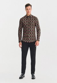 Długi rękaw, dopasowana koszula w kolorze czarnym z misternymi kwiatowymi wzorami w odcieniach różowym i zielonym. Połączona z czarnymi spodniami i błyszczącymi butami eleganckimi.